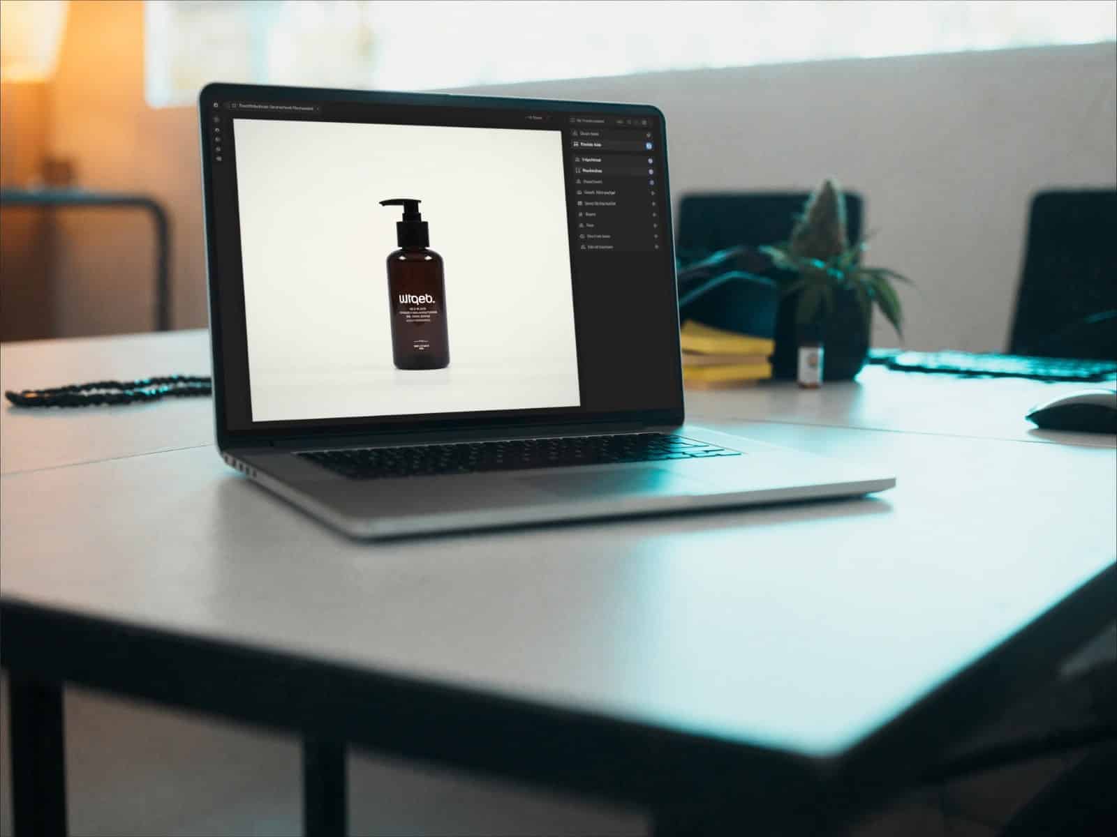 Laptop auf hellem Schreibtisch mit Produktfoto einer Flasche auf dem Bildschirm, Cannabispflanze unscharf im Hintergrund